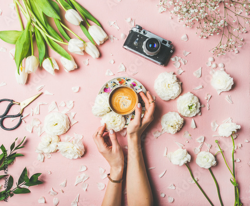 Spring colorful layout. Flat-lay of female hands holding cup of coffee, scissors, film camera, white tulips and buttercup flowers over pink background, top view. Spring or Women's Day holiday concept photo