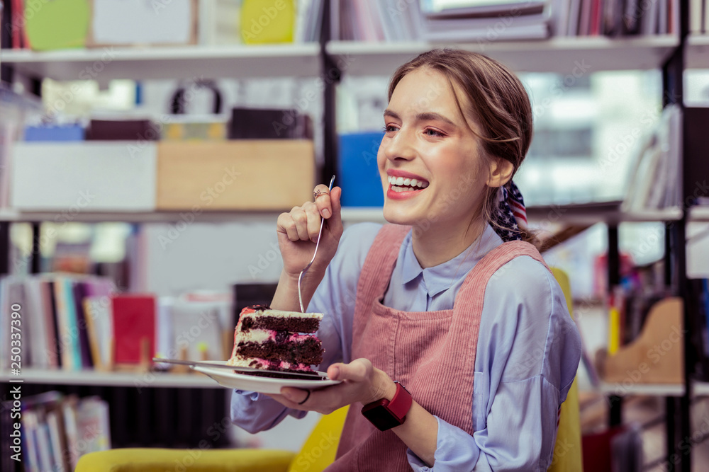 Laughing appealing girl separating piece of cake with fork