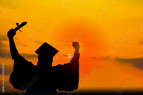 Silhouette photo.He is  wearing  graduate's dress. He is standing and show hand. He is celebration education Graduation . He is happy in good time. 