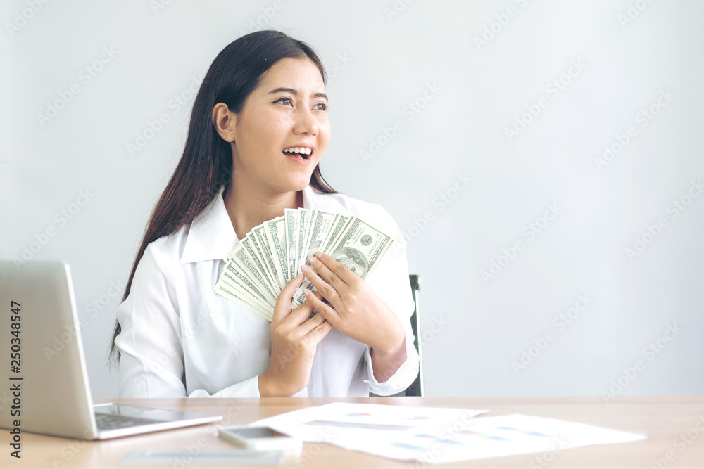 Successful beautiful Asian business young woman holding money US dollar bills in hand on office desk, business concept Successful beautiful Asian business young woman holding money US dollar bills in hand on office desk, business concept