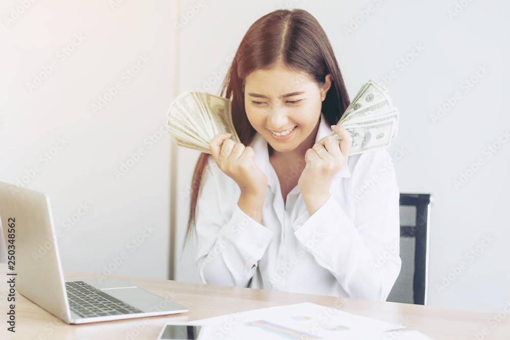 Successful beautiful Asian business young woman holding money US dollar bills in hand on office desk, business concept Successful beautiful Asian business young woman holding money US dollar bills in hand on office desk, business concept
