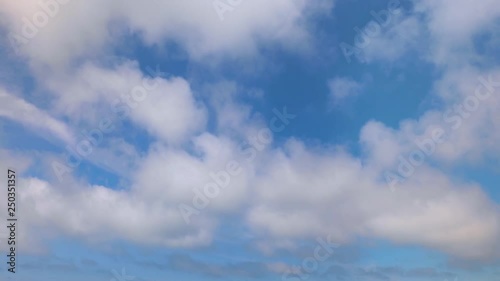 Looping one minute footage features white puffy clouds on a sunny day moving across a deep blue sky.