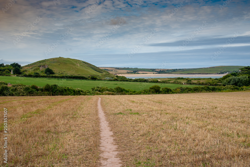 Path across a harvested field with Brea Hill and the Camel Estuary in the background in Cornwall, UK.