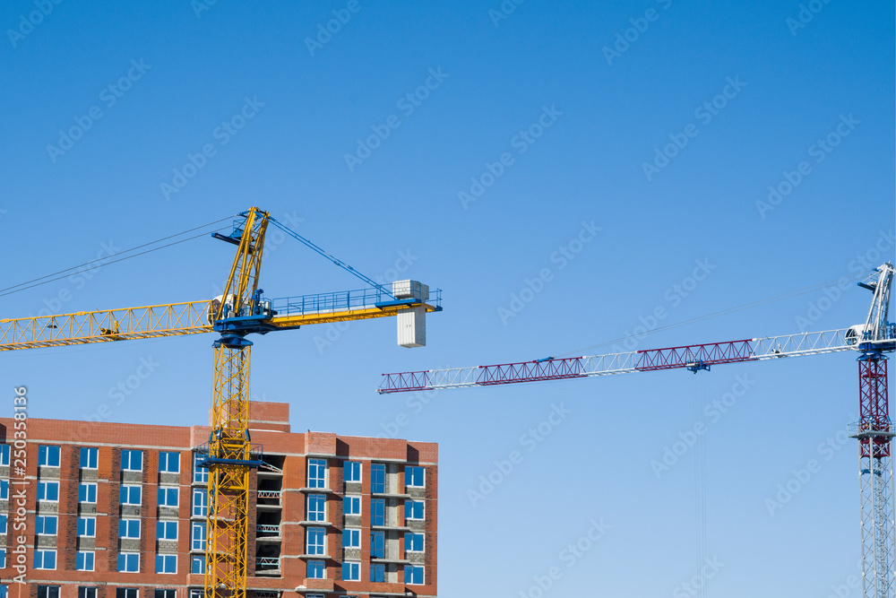 Multi-storey construction.  Unfinished multi-storey building. Next to the building-two cranes on the background of the blue sky. Copy space.