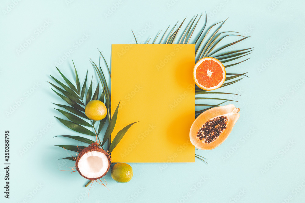 Fototapeta Summer composition. Tropical palm leaves, fruits, yellow paper blank on pastel blue background. Summer concept. Flat lay, top view, copy space