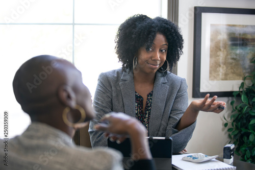 Black female client is upset at tax preparer or CPA accountant in an office.  The image can also depict a manager angry at a secretary.