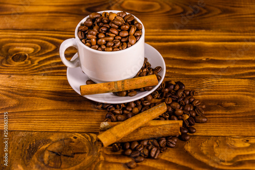 White cup filled with coffee beans and cinnamon sticks on wooden table