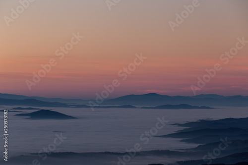 Beautifully colored sky at dusk, with mountains layers over a sea of fog © Massimo