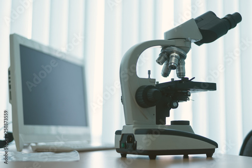 Microscope and a computer on a table in a laboratory on a window light background.