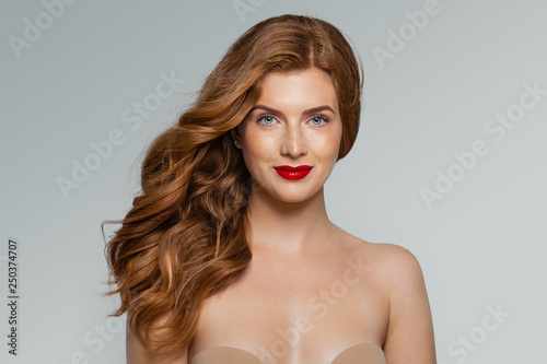 Young red-haired smiling woman against white wall background