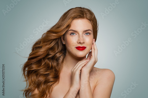 Stylish attractive young redhead woman looking at camera on blue background