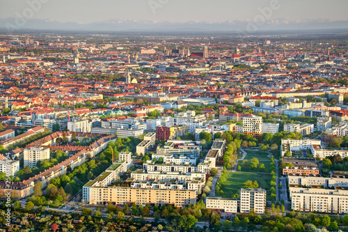 Aerial view of city outskirts and historic center with sunlit apartment buildings, housing estates, green parks, church towers and snowy Bavarian Alps in background Munchen Bayern Germany Europe photo