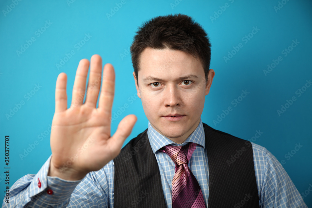 Young businessman in suit on blue background holds his hand in front of him, stop sign. Young businessman in suit on blue background holds his hand in front of him, stop sign.