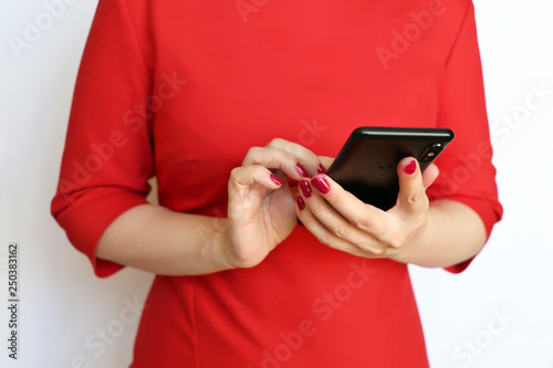 Slim girl in red dress with smartphone in manicured hands on white background. Concept of business woman, online communication, text messaging