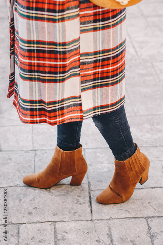 Fashion blogger outfit details. Fashionable woman wearing a plaid overcoat, black jeans and camel ankle shoes. Detail of a perfect fall or winter fashion outfit. Vertical image.