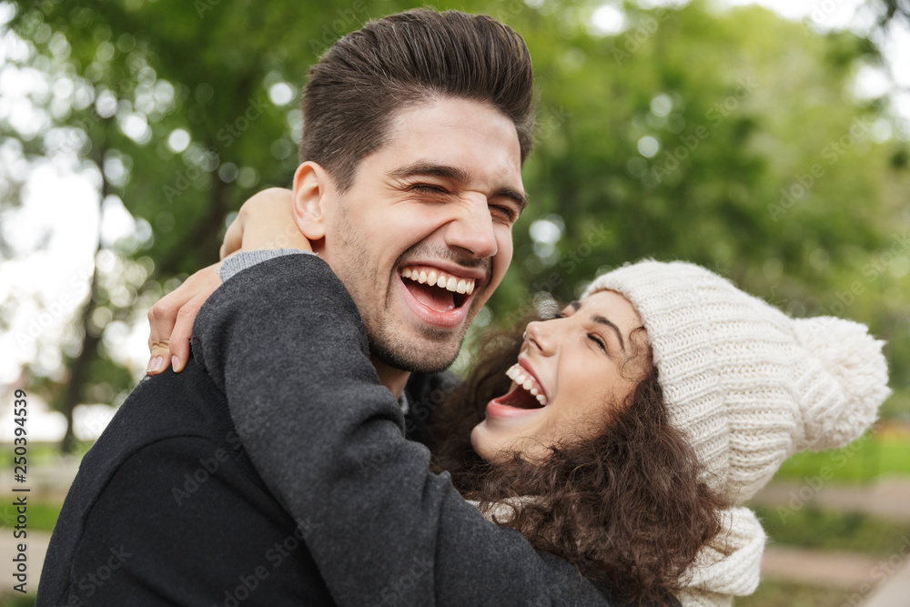 Portrait closeup of smiling people man and woman 20s hugging and laughing, while walking through green park Portrait closeup of smiling people man and woman 20s hugging and laughing, while walking through green park