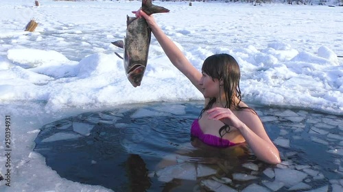 Woman winter swims in icy water. She is fishing.