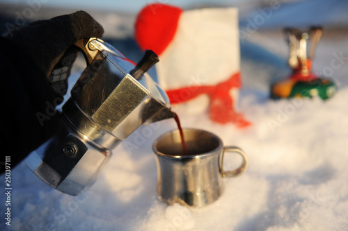 Coffee brewing in moka pot on a gas burner on the car trunk outdoor in winter snow landscape.