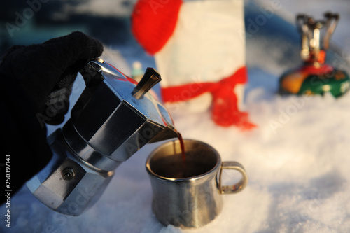 Coffee brewing in moka pot on a gas burner on the car trunk outdoor in winter snow landscape.