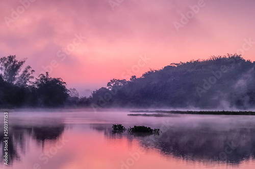 sunrise at Chiang Saen Lake, beautiful lake view misty morning of the hill around with soft mist moving above the water and colorful sun light in the sky background, Chiang Rai, northern of Thailand.