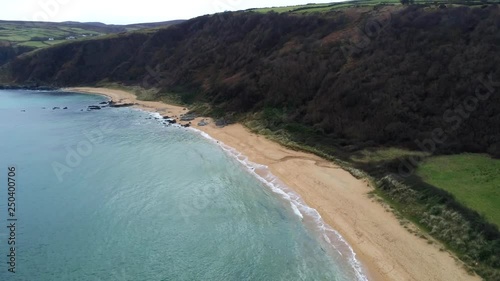 This is an aerial video over Kinnagoe bay in Ireland.  The footage is a wide angel high up aerial shoot of the beach.  You see white sand and turquoise clear ocean