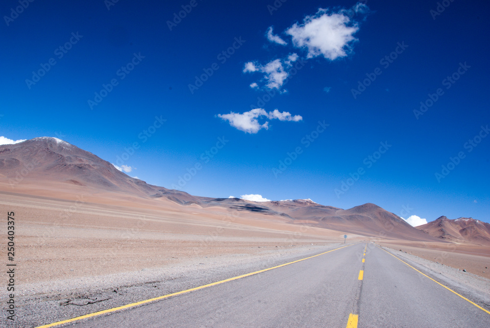 empty desert highway surrounded by mountains with a clear blue sky