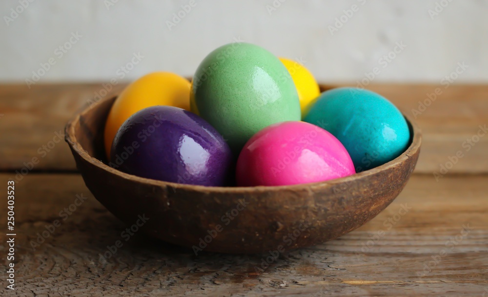 Colorful easter eggs in a brown bowl. Wooden table, light backgroun, close up Colorful easter eggs in a brown bowl. Wooden table, light backgroun, close up