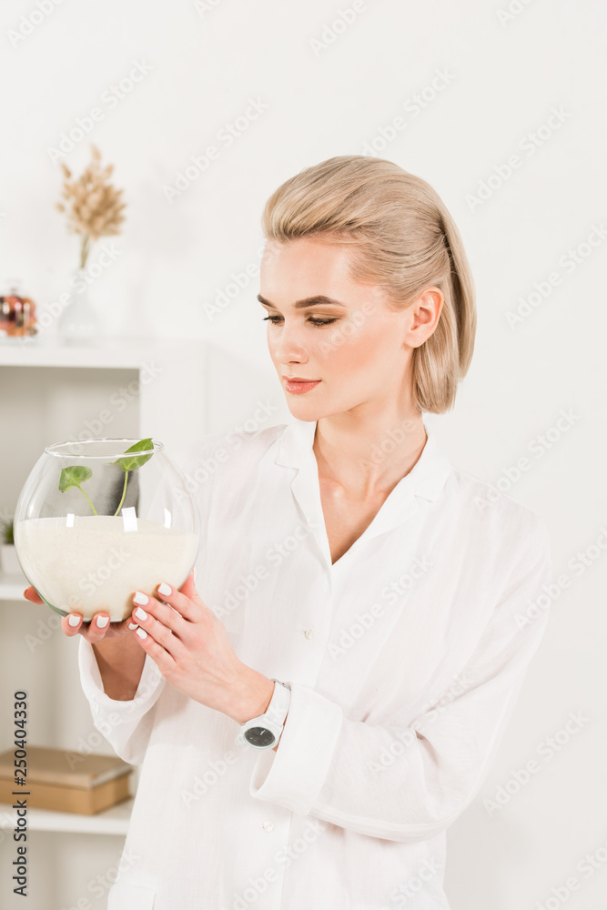beautiful woman looking at glass fish bowl with sand and green small leaves, environmental saving concept beautiful woman looking at glass fish bowl with sand and green small leaves, environmental saving concept