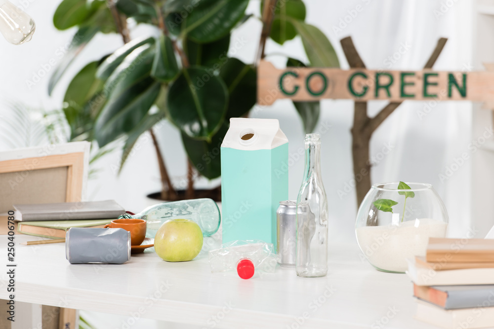 selective focus of glass bottles cans and paper milk package near wooden sign with go green lettering, environmental saving concept selective focus of glass bottles cans and paper milk package near wooden sign with go green lettering, environmental saving concept