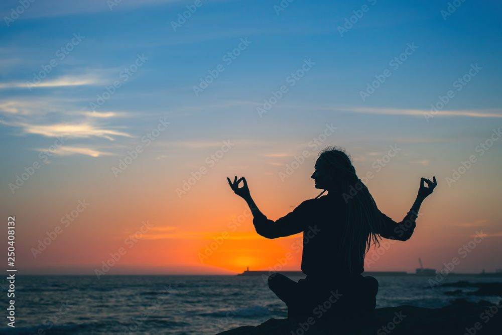 Yoga woman meditation silhouette. Healthy lifestyle on the ocean during amazing sunset.