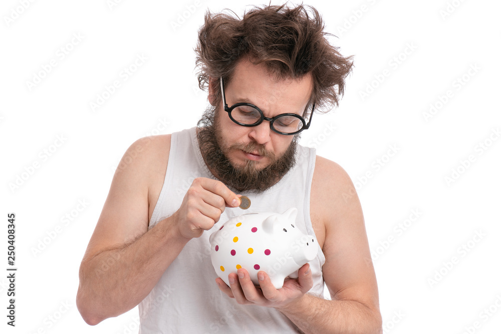 Crazy bearded Man with funny Haircut in eye Glasses holding Piggy Bank and coin, isolated on white background. Saving Money concept. Male putting coin in his piggybank. Crazy bearded Man with funny Haircut in eye Glasses holding Piggy Bank and coin, isolated on white background. Saving Money concept. Male putting coin in his piggybank.