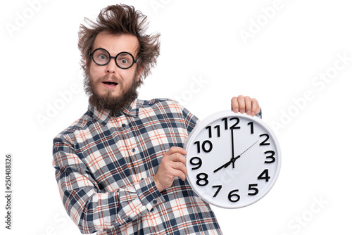 Crazy bearded Man in plaid shirt with funny Haircut in eye Glasses holding Big Clock, isolated on white background. Time concept.