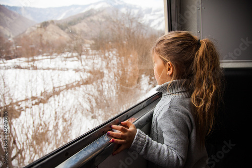 Little girl in grey sweater travelling by Kukushka train in Georgia and looking throught the window photo