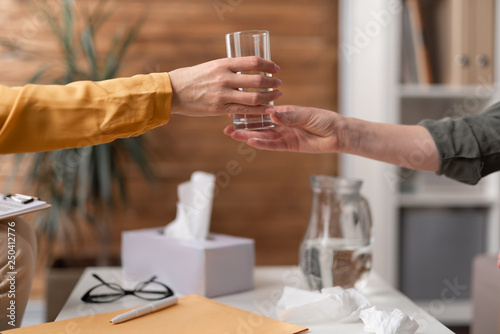 Psychologist is giving glass with water to her patient over the table