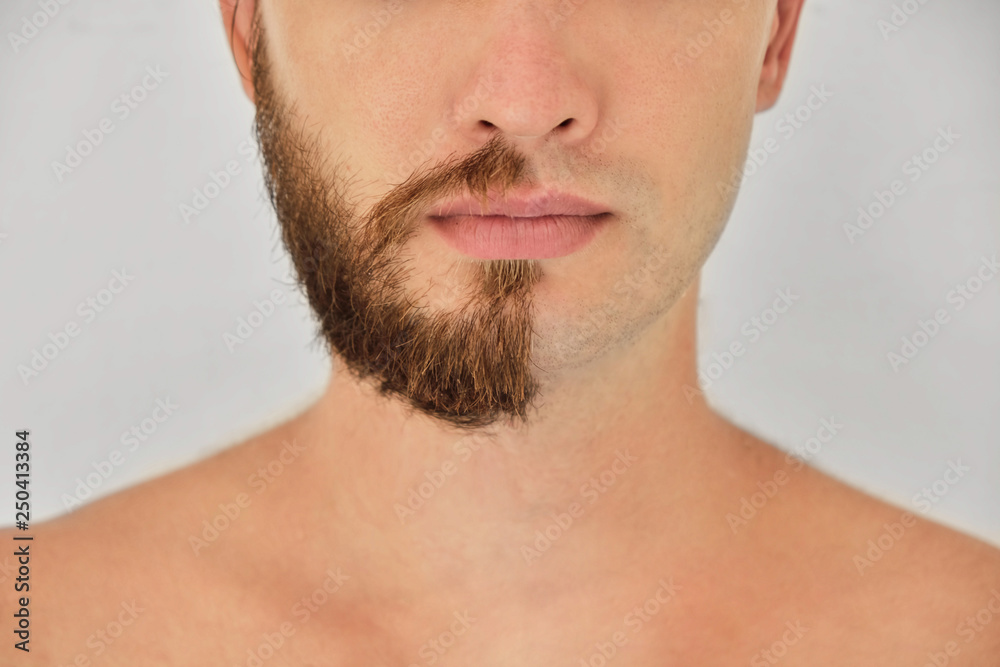 A young man with a beard on half of the face on light grey background A young man with a beard on half of the face on light grey background
