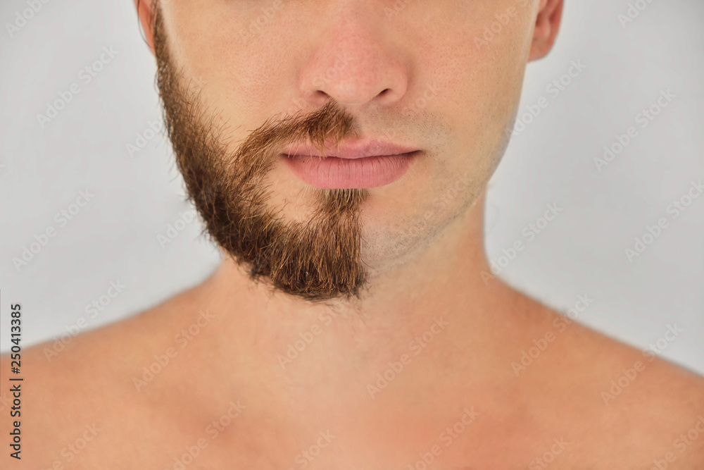 A young man with a beard on half of the face on light grey background A young man with a beard on half of the face on light grey background