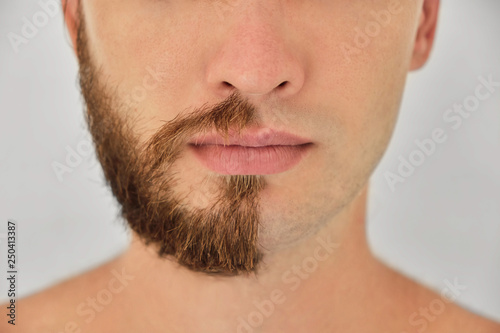 A young man with a beard on half of the face on light grey background
