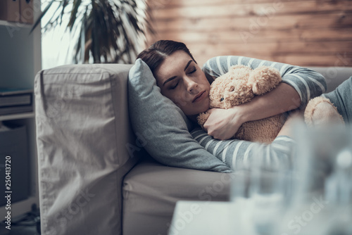 Brunette Caucasian sleepy woman lying on sofa with toy in arms