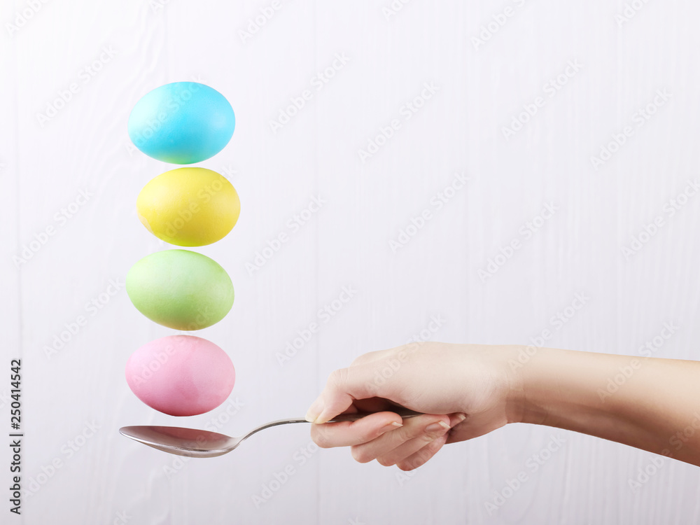 Female hand holds a spoon on which multi-colored eggs are balanced, on a white background. Unusual design, Easter concept, copy space. Female hand holds a spoon on which multi-colored eggs are balanced, on a white background. Unusual design, Easter concept, copy space.