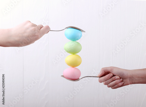 Female hand holds a spoon on which multi-colored eggs are balanced  on a white background. Unusual design  Easter concept  copy space.