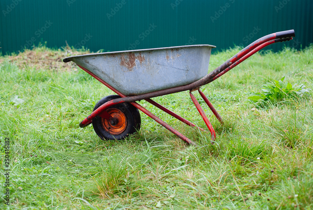 Wheelbarrow on green grass lawn in a farm garden Wheelbarrow on green grass lawn in a farm garden