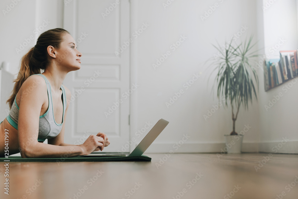 Obraz premium Dreamful female laying on yoga mat with laptop