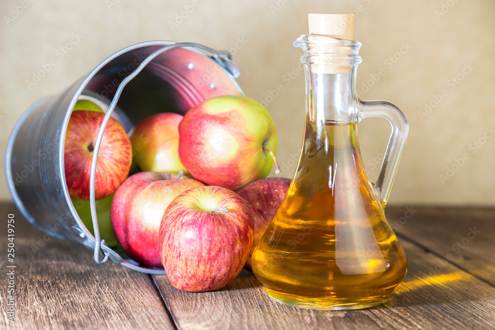 Processing of an agricultural crop of red and green apples. Home canning, healthy diet vegetarian food. Apple cider vinegar, juice, cider in a glass jug next to a bucket of ripe fruit Processing of an agricultural crop of red and green apples. Home canning, healthy diet vegetarian food. Apple cider vinegar, juice, cider in a glass jug next to a bucket of ripe fruit