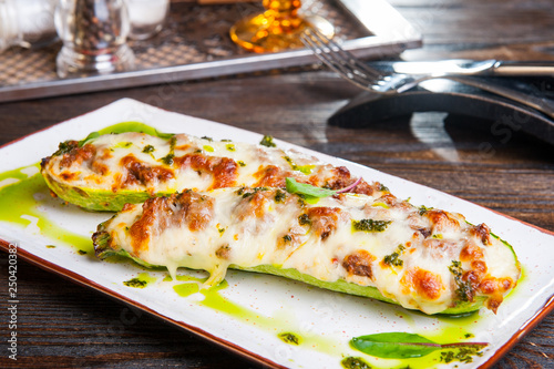 Close up Baked stuffed zucchini boats. Zucchini stuffed with meat and cheese and pesto sauce served on the white plate on the dark wooden table. Healthy food concept.