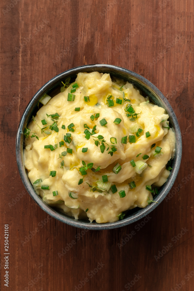 Pomme puree, a bowl of mashed potatoes with herbs, shot from above on a dark rustic wooden background with a place for text Pomme puree, a bowl of mashed potatoes with herbs, shot from above on a dark rustic wooden background with a place for text