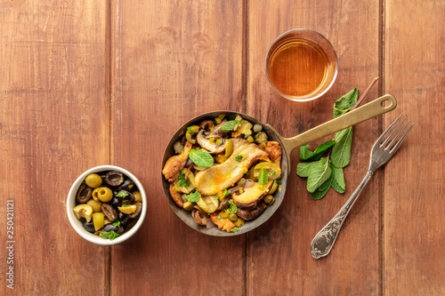 An overhead photo of a rustic mushrooms and olives saute with mint, a glass of white wine, and a place for text