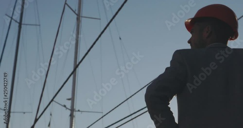 backside close view man in helmet silhouette against yacht masts and bright sun disk light in clear blue sky