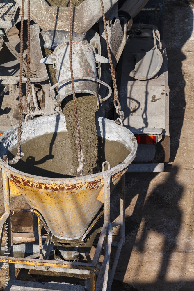 Fototapeta premium Construction workers pouring wet concrete using concrete bucket