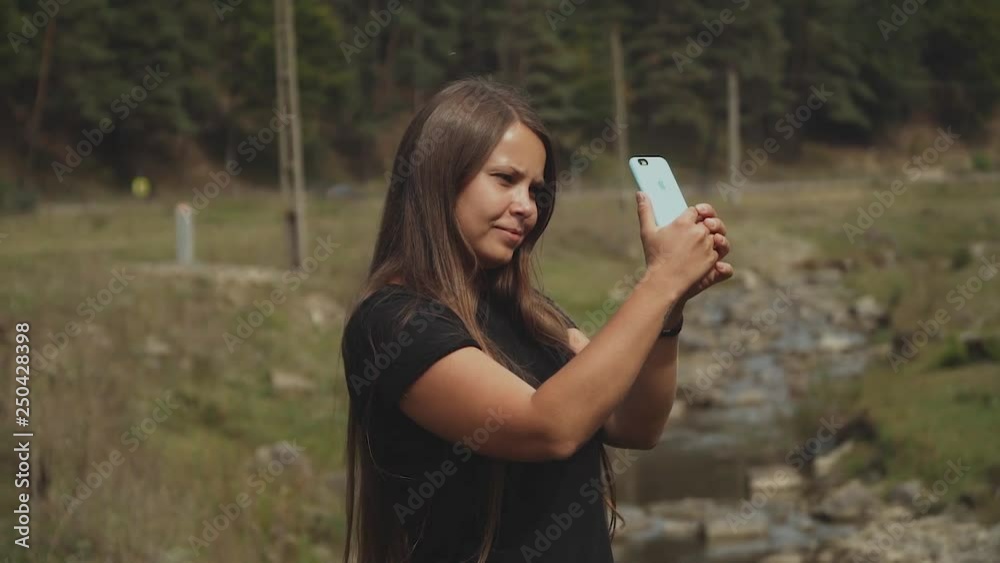 Young woman with long hair walking and taking photo in the pine tree forest near small river,slow motion.Mountains of Romania. Young woman with long hair walking and taking photo in the pine tree forest near small river,slow motion.Mountains of Romania.