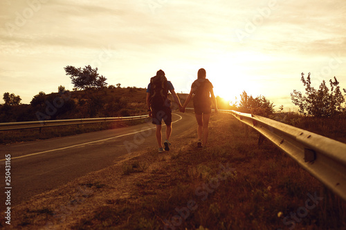 Travelers with backpacks go on the road at sunset.